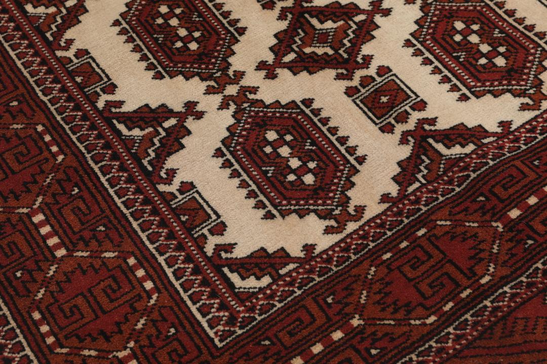 Een handgeknoopt Turkaman-tapijt met geometrische medaillons in rode en beige tinten.