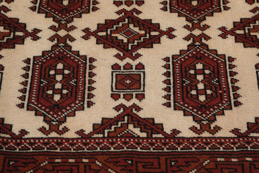Een handgeknoopt Turkaman-tapijt met geometrische medaillons in rode en beige tinten.