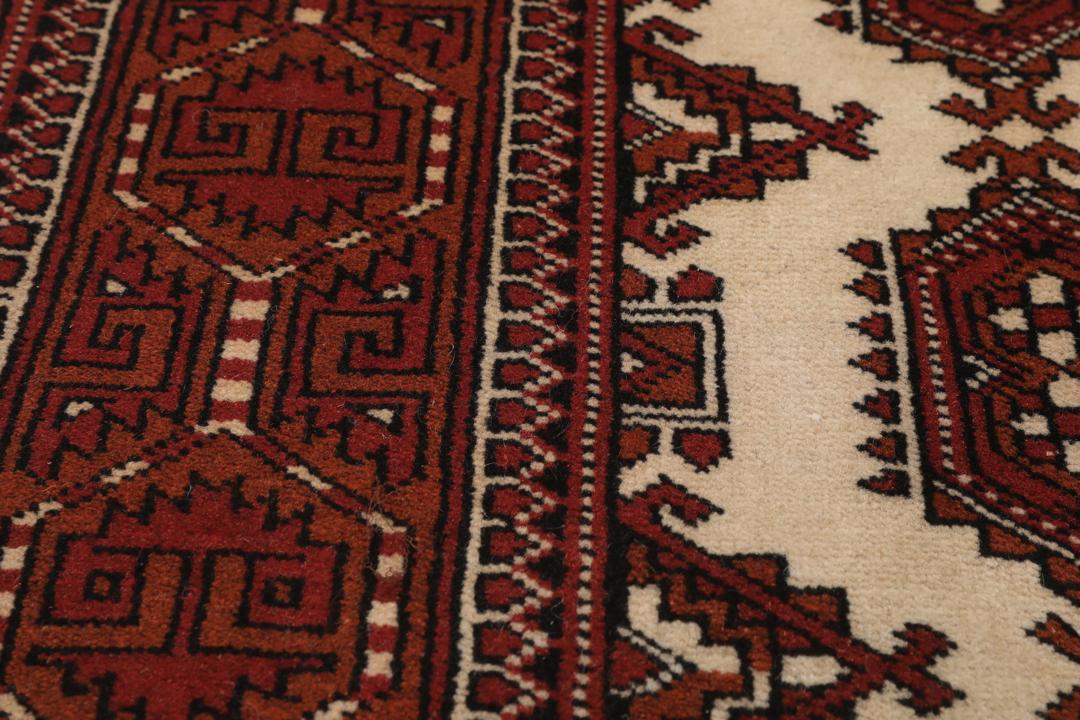Een handgeknoopt Turkaman-tapijt met geometrische medaillons in rode en beige tinten.