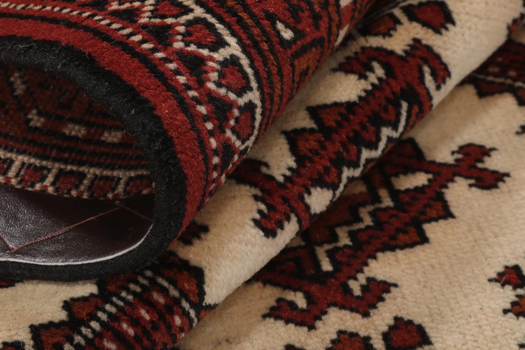 Een handgeknoopt Turkaman-tapijt met geometrische medaillons in rode en beige tinten.