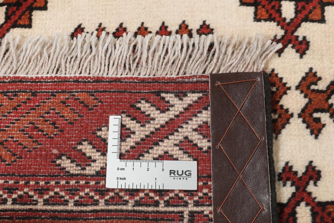 Een handgeknoopt Turkaman-tapijt met geometrische medaillons in rode en beige tinten.