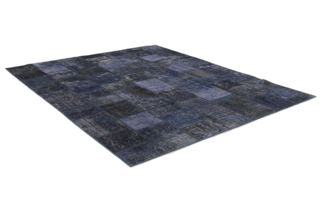 Een groot rechthoekig patchwork tapijt met verschillende blauwtinten en ingewikkelde patronen van oorsprong uit het Midden-Oosten.