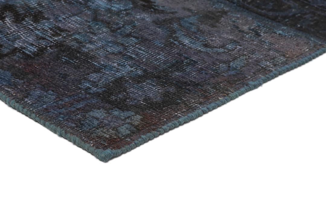 Een groot rechthoekig patchwork tapijt met verschillende blauwtinten en ingewikkelde patronen van oorsprong uit het Midden-Oosten.