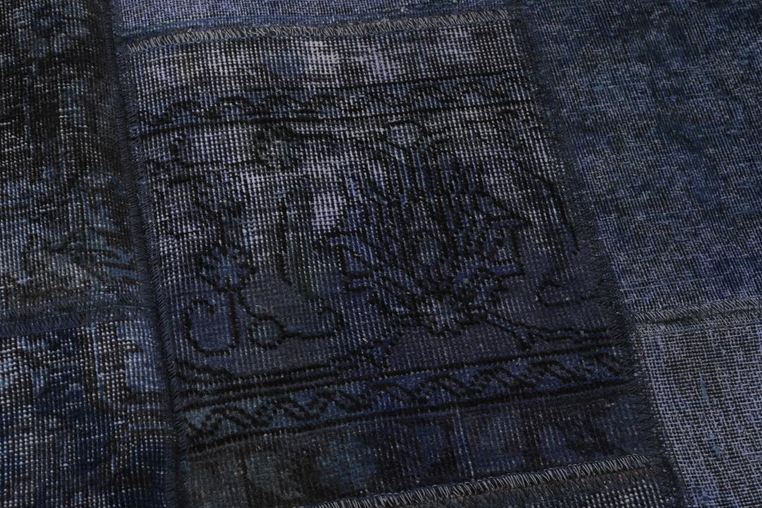 Een groot rechthoekig patchwork tapijt met verschillende blauwtinten en ingewikkelde patronen van oorsprong uit het Midden-Oosten.
