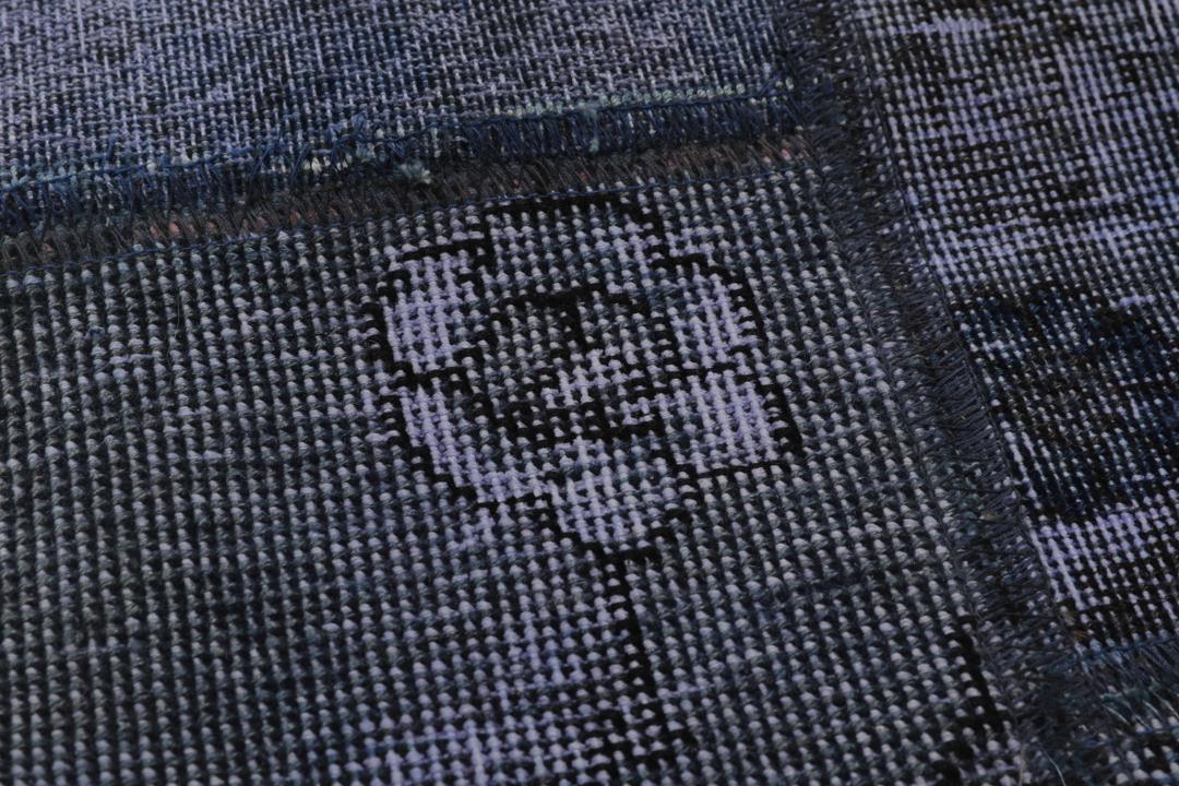 Een groot rechthoekig patchwork tapijt met verschillende blauwtinten en ingewikkelde patronen van oorsprong uit het Midden-Oosten.
