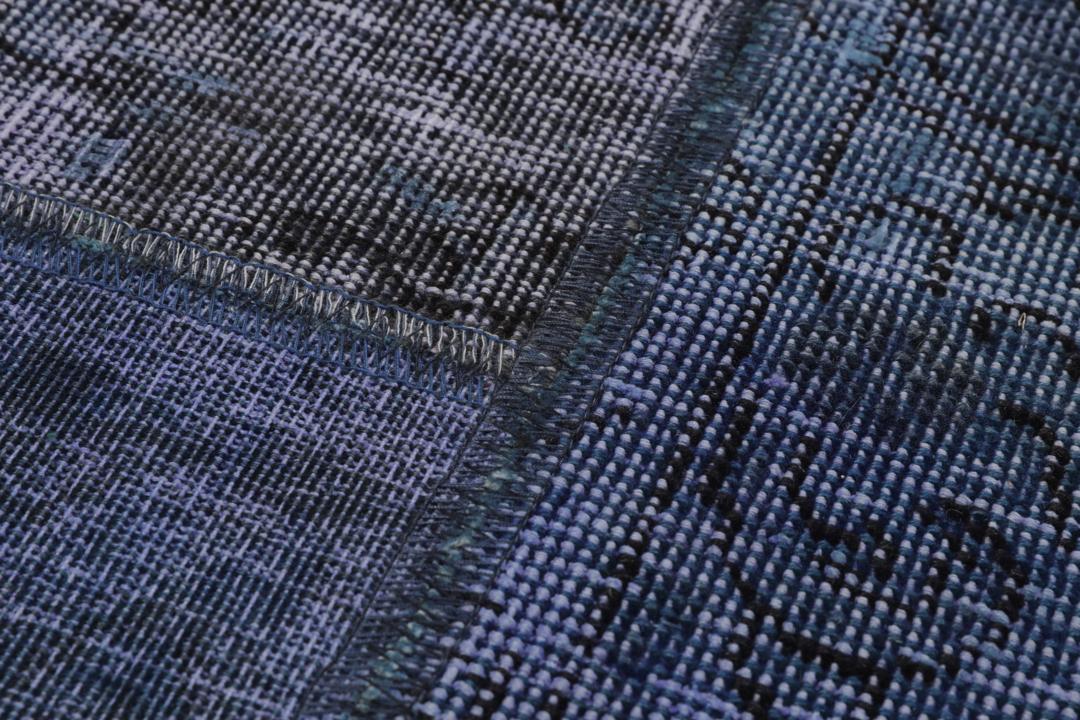 Een groot rechthoekig patchwork tapijt met verschillende blauwtinten en ingewikkelde patronen van oorsprong uit het Midden-Oosten.