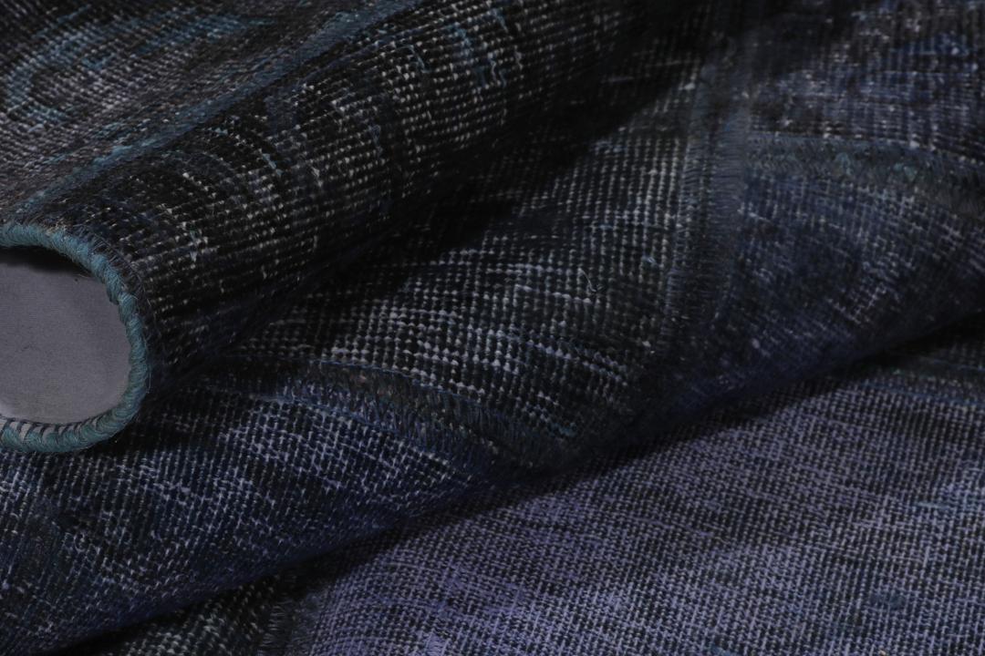 Een groot rechthoekig patchwork tapijt met verschillende blauwtinten en ingewikkelde patronen van oorsprong uit het Midden-Oosten.