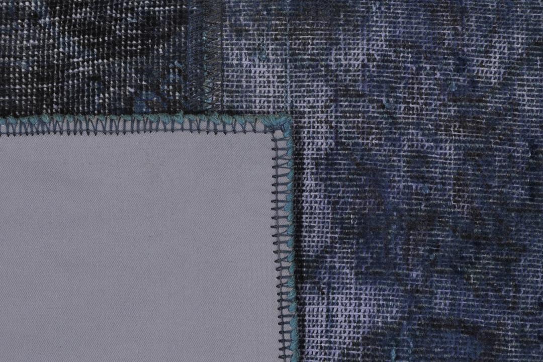 Een groot rechthoekig patchwork tapijt met verschillende blauwtinten en ingewikkelde patronen van oorsprong uit het Midden-Oosten.