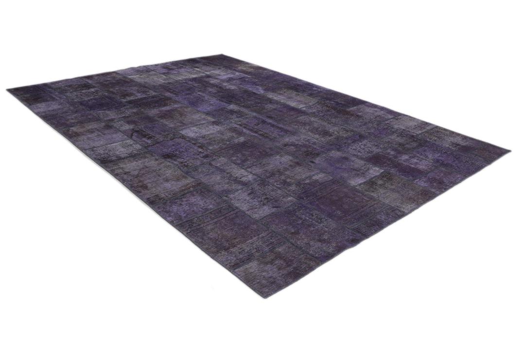 Een groot, handgeknoopt patchwork vloerkleed met ingewikkelde patronen in diepe donkerpaarse tinten.
