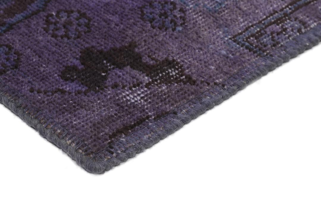 Een groot, handgeknoopt patchwork vloerkleed met ingewikkelde patronen in diepe donkerpaarse tinten.