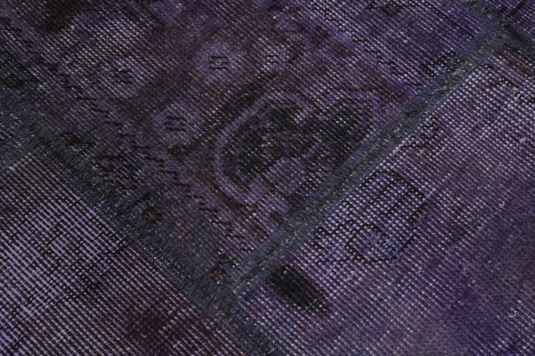 Een groot, handgeknoopt patchwork vloerkleed met ingewikkelde patronen in diepe donkerpaarse tinten.