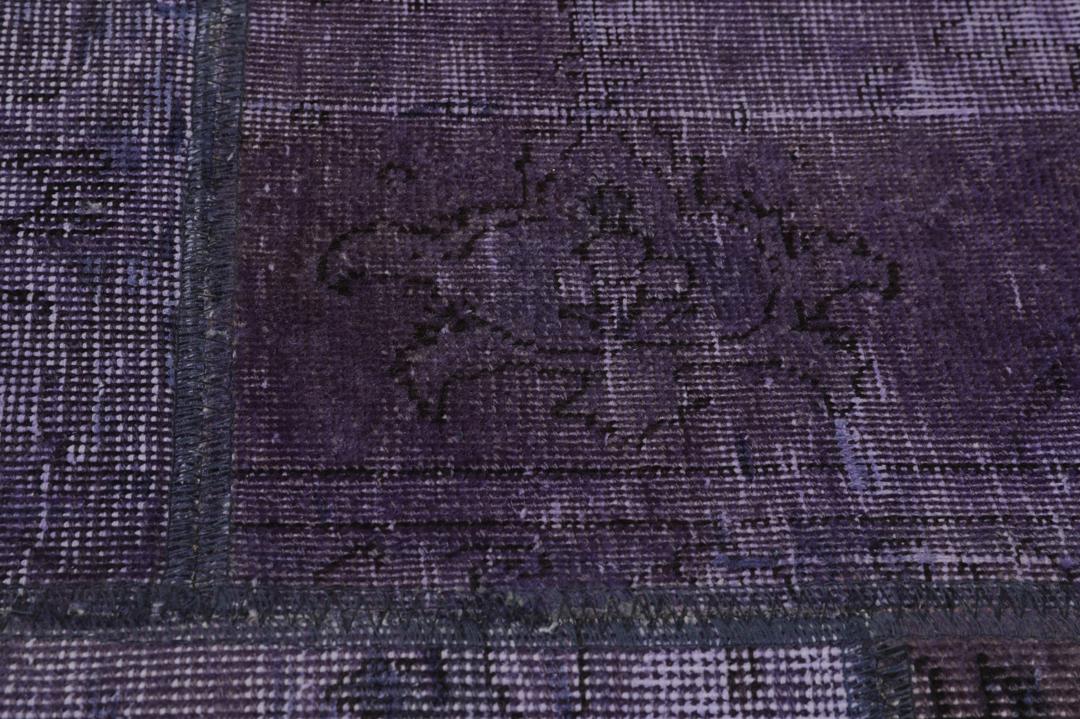Een groot, handgeknoopt patchwork vloerkleed met ingewikkelde patronen in diepe donkerpaarse tinten.