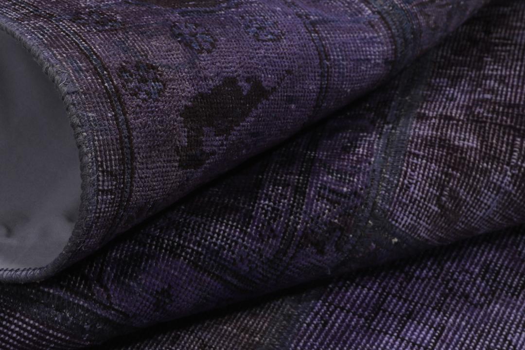 Een groot, handgeknoopt patchwork vloerkleed met ingewikkelde patronen in diepe donkerpaarse tinten.