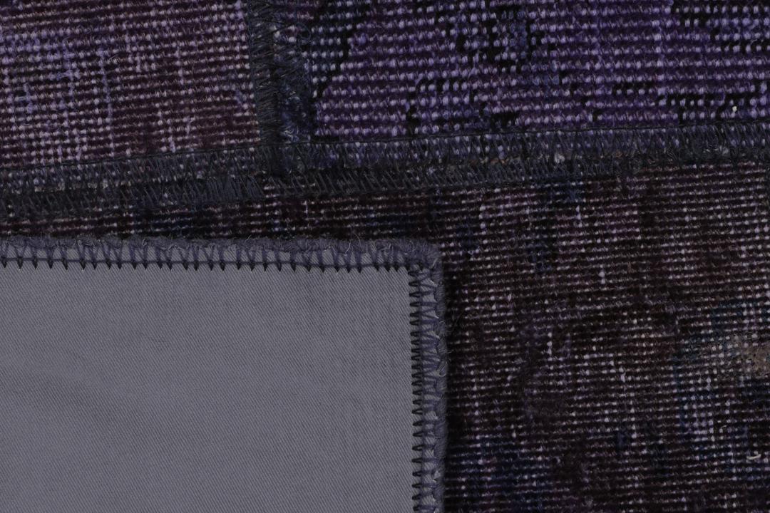Een groot, handgeknoopt patchwork vloerkleed met ingewikkelde patronen in diepe donkerpaarse tinten.