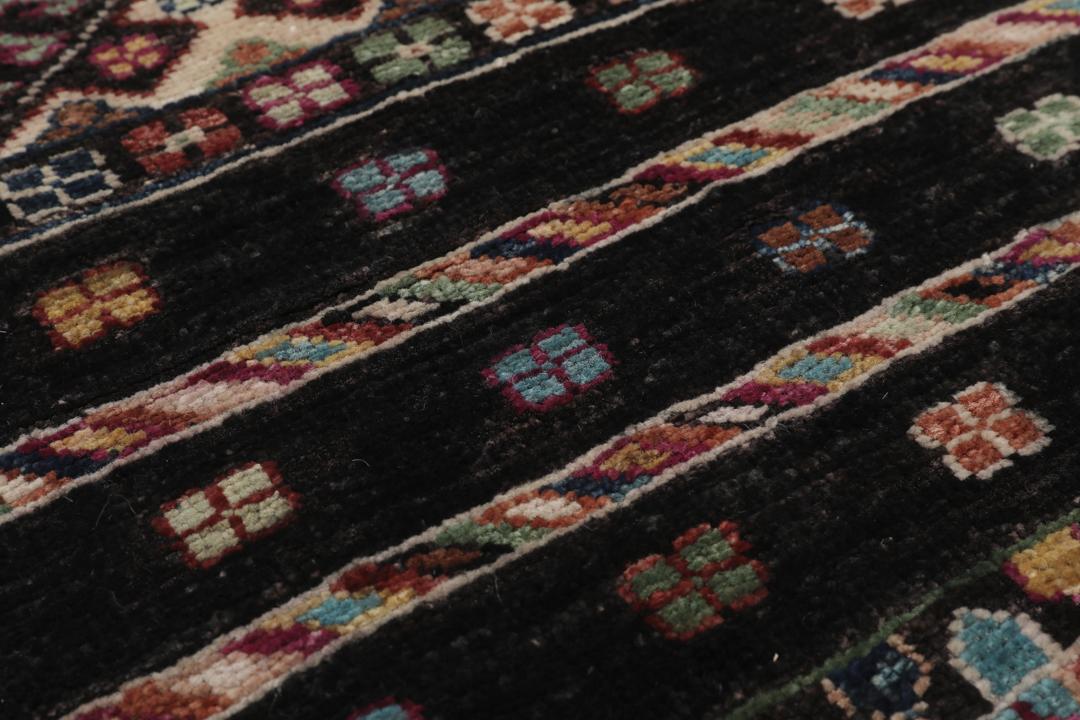 Alfombra afgana anudada a mano con patrones geométricos multicolores sobre fondo negro