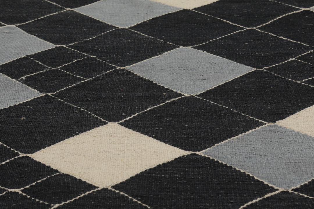 Een modern Afghaans Kelim-tapijt met een geometrisch ruitpatroon in zwart, grijs en beige.