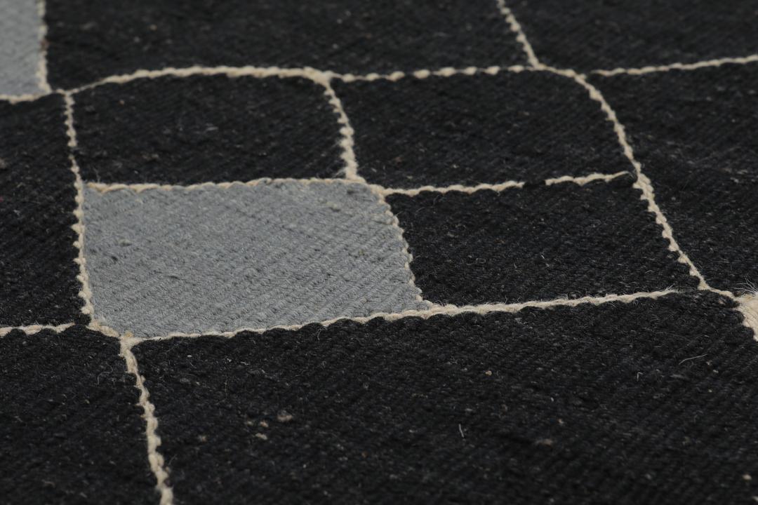 Een modern Afghaans Kelim-tapijt met een geometrisch ruitpatroon in zwart, grijs en beige.