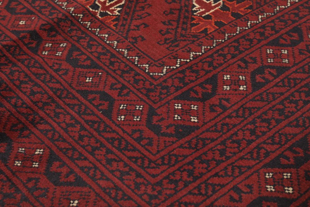 Een handgeknoopt Kunduz-tapijt uit Afghanistan met een donkerrood veld en geometrische patronen.