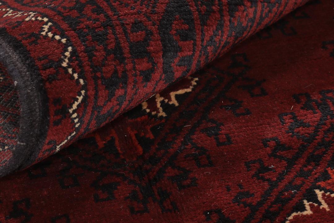 Een handgeknoopt Kunduz-tapijt uit Afghanistan met een donkerrood veld en geometrische patronen.