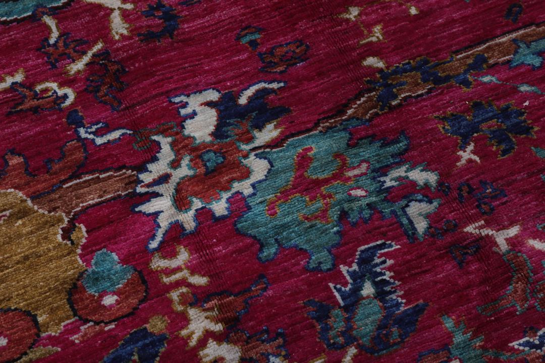 Un tapis afghan vibrant avec des motifs figuratifs dans des tons roses et bleus.
