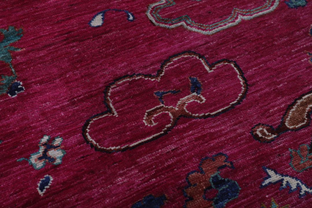 Un tapis afghan vibrant avec des motifs figuratifs dans des tons roses et bleus.