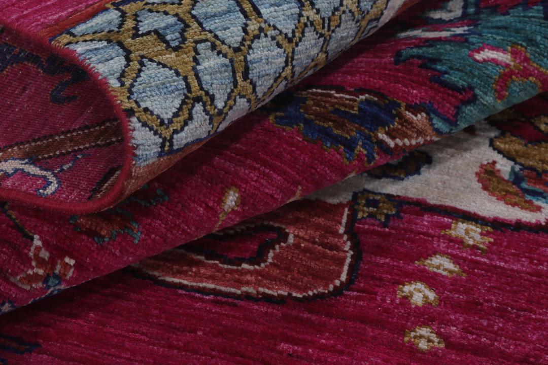 Un tapis afghan vibrant avec des motifs figuratifs dans des tons roses et bleus.