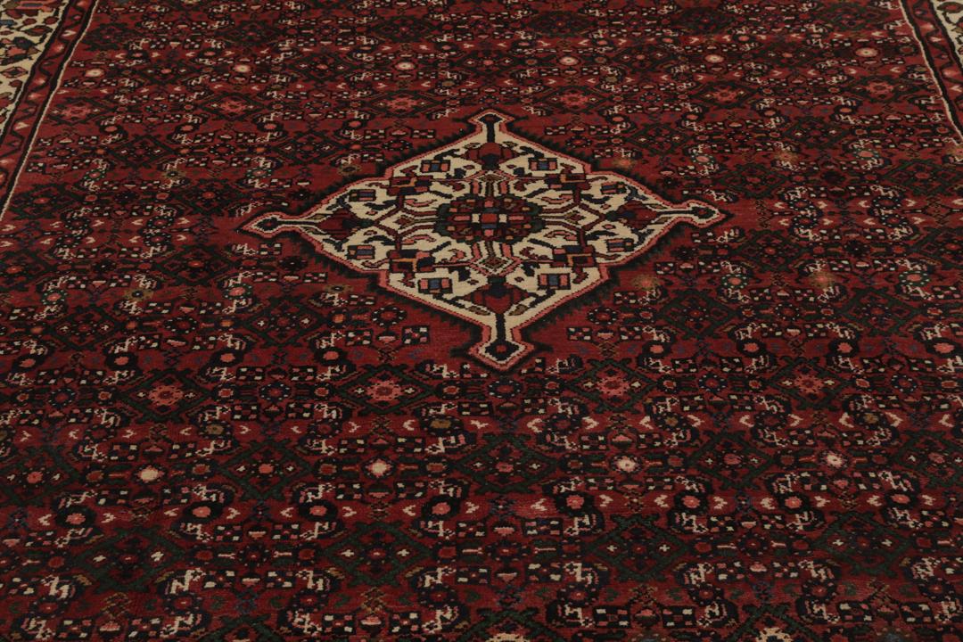 Et håndknyttet Hosseinabad-tæppe fra Mellemøsten i dybe mørkerøde toner.