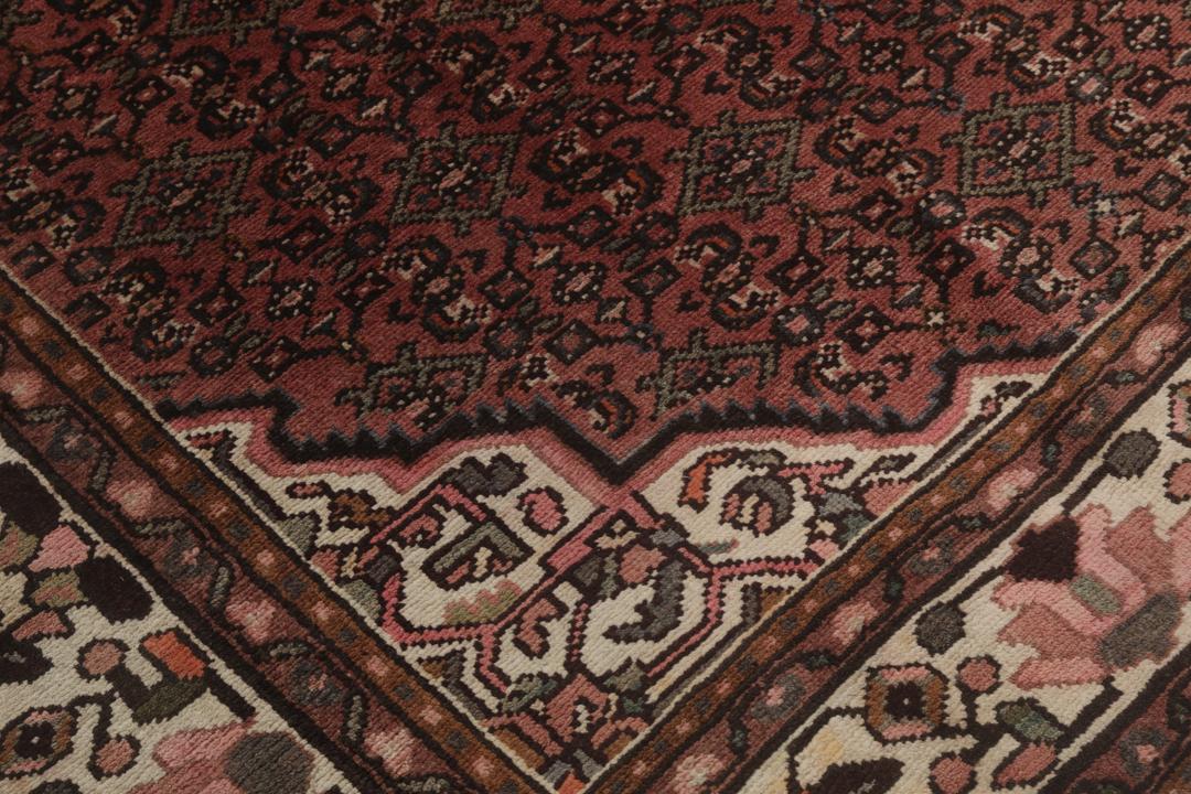 Et håndknyttet Hosseinabad-tæppe fra Mellemøsten med et mørkerødt felt.