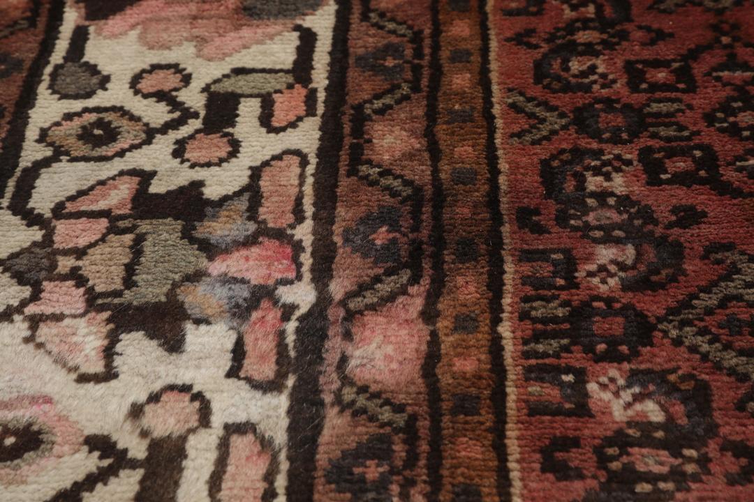 Et håndknyttet Hosseinabad-tæppe fra Mellemøsten med et mørkerødt felt.