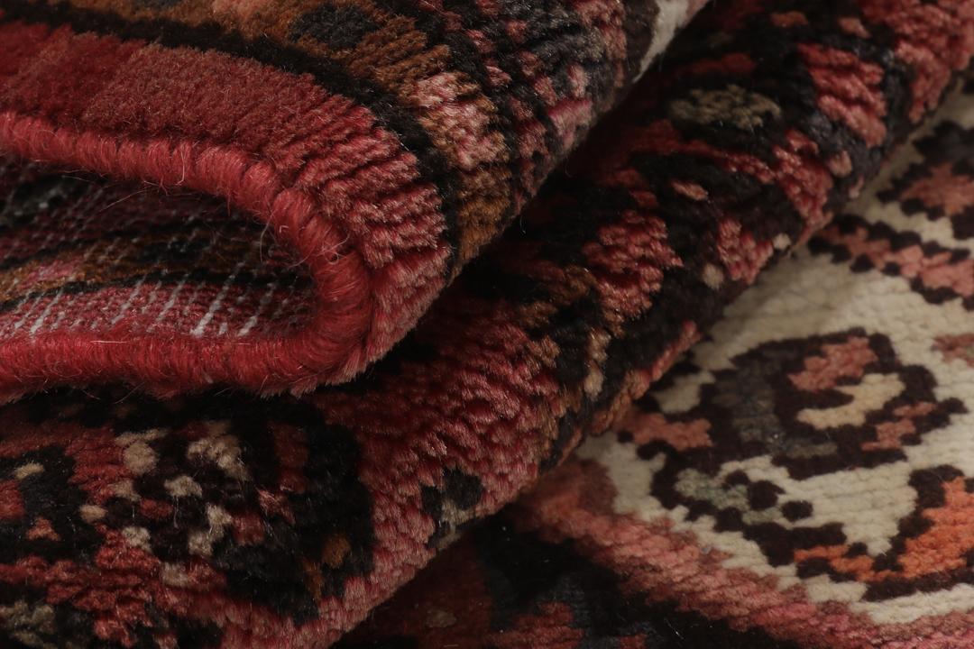 Et håndknyttet Hosseinabad-tæppe fra Mellemøsten med et mørkerødt felt.