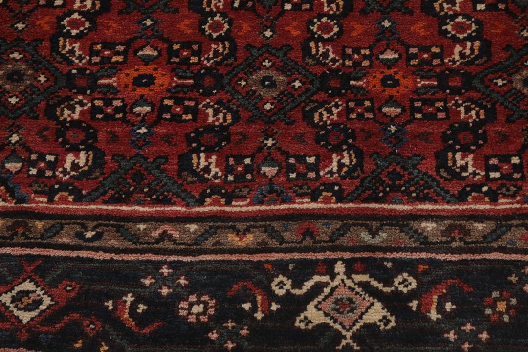 A large hand-knotted Hosseinabad rug from the Middle East featuring red and dark blue tones.