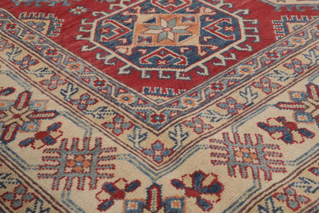 Un covor Kazak afgan înnodat manual cu un câmp roșu și modele de medalioane geometrice.