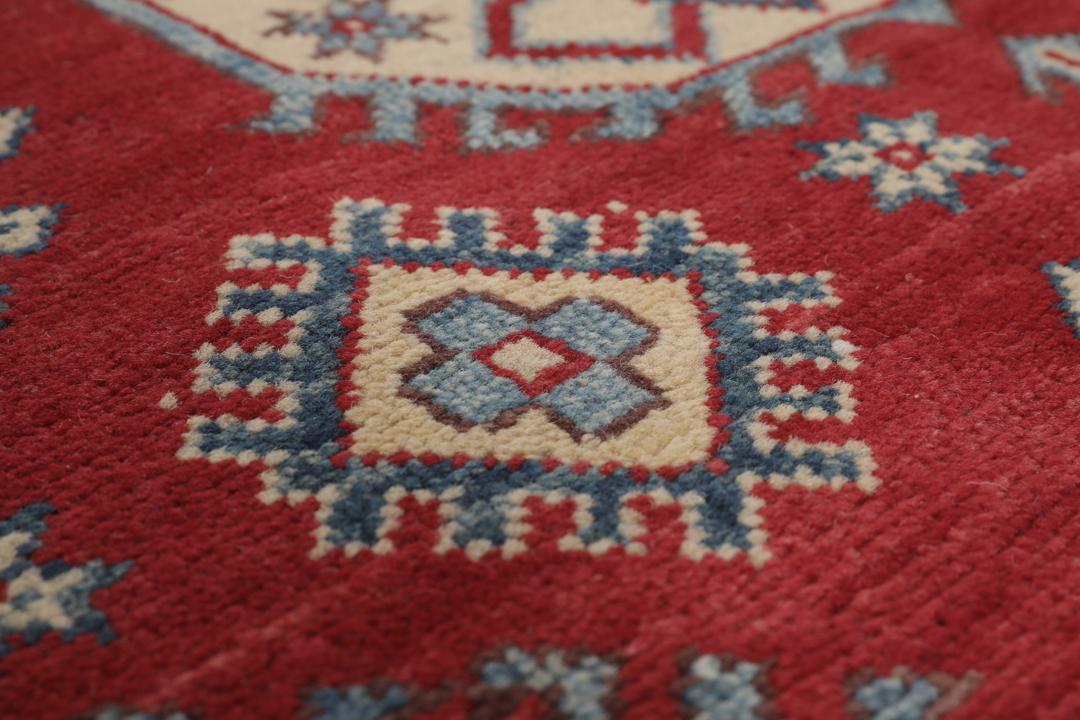 Un covor Kazak afgan înnodat manual cu un câmp roșu și modele de medalioane geometrice.