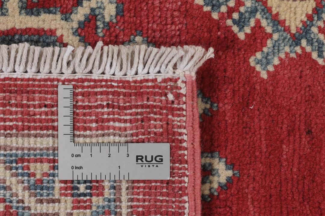 Un covor Kazak afgan înnodat manual cu un câmp roșu și modele de medalioane geometrice.