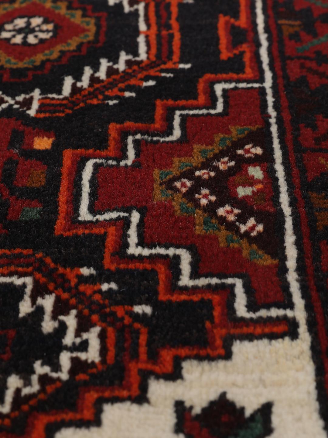 Handgeknoopt Beluch-tapijt met geometrische motieven in donkerrode en zwarte tinten.