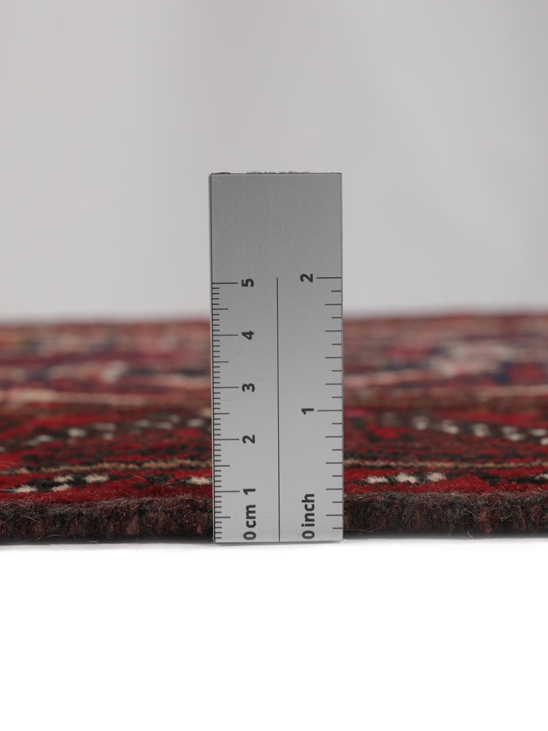 Håndknyttet mellemøstligt tæppe i dybe røde og mørke toner med geometriske motiver.