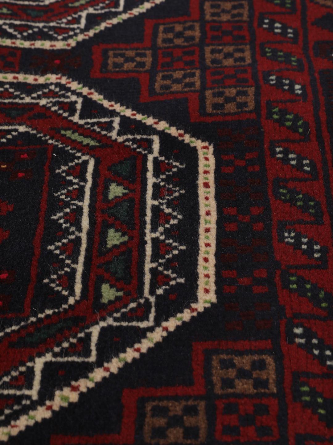Et håndknyttet Beluch-tæppe fra Mellemøsten i dybe mørkerøde toner med geometriske motiver.