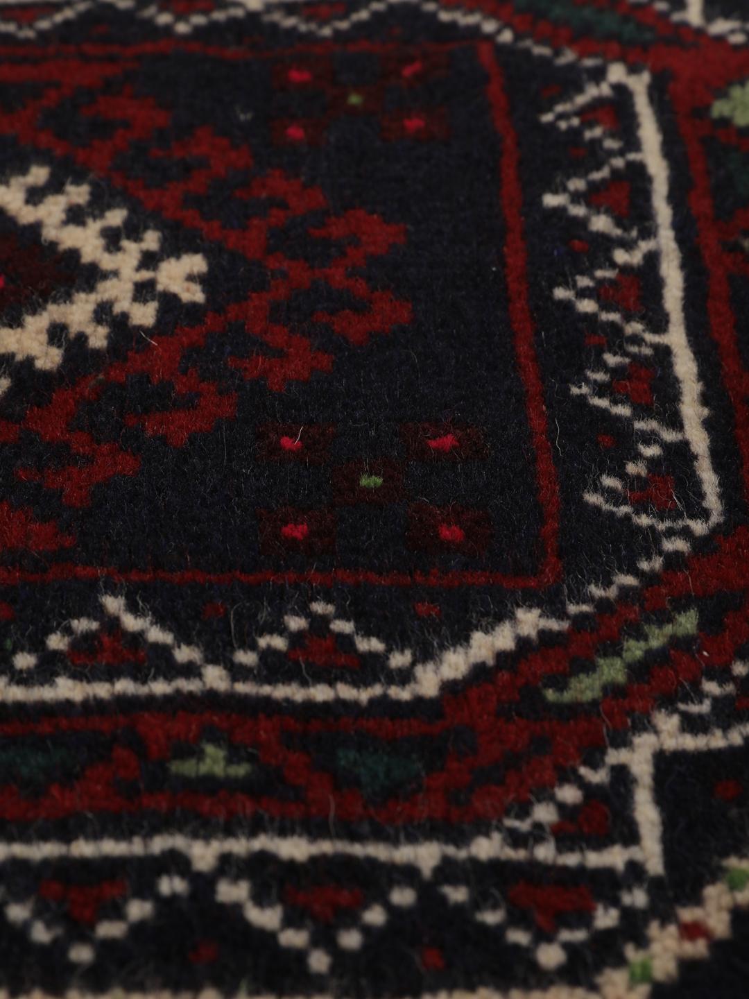 Et håndknyttet Beluch-tæppe fra Mellemøsten i dybe mørkerøde toner med geometriske motiver.