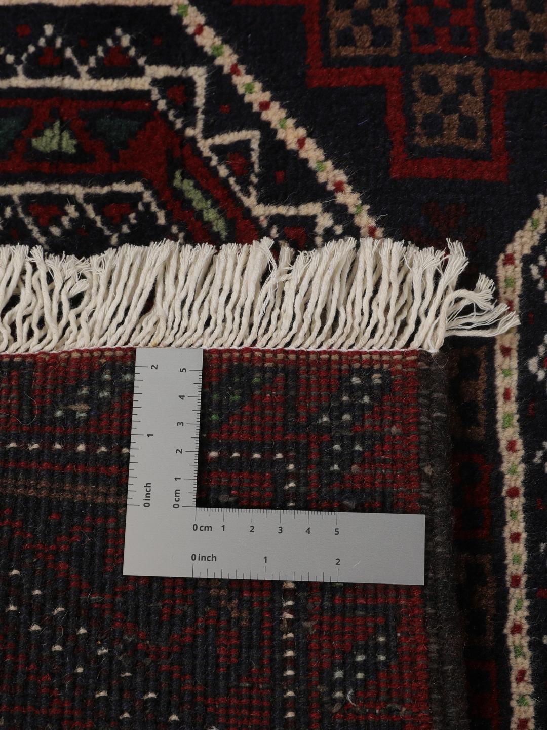 Et håndknyttet Beluch-tæppe fra Mellemøsten i dybe mørkerøde toner med geometriske motiver.