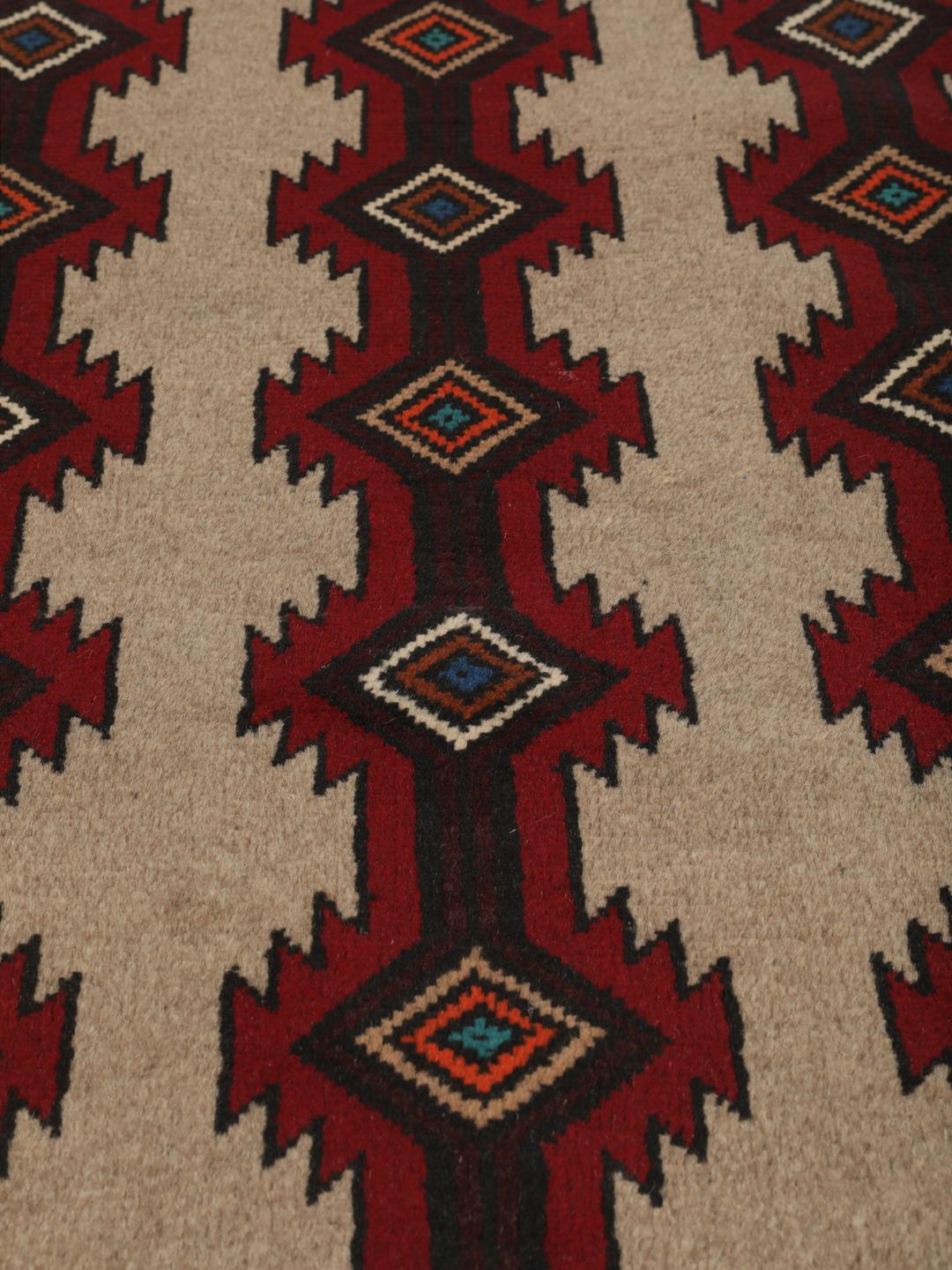 Een handgeknoopt Baluch tapijt uit het Midden-Oosten met een geometrisch patroon in rood en beige.