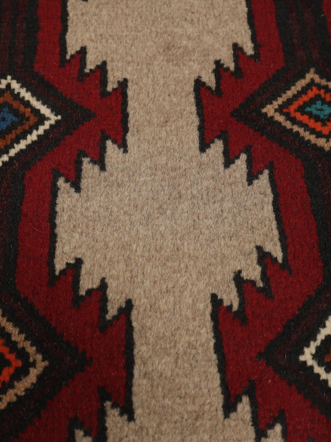 Een handgeknoopt Baluch tapijt uit het Midden-Oosten met een geometrisch patroon in rood en beige.