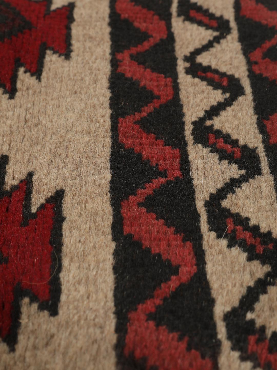 Een handgeknoopt Baluch tapijt uit het Midden-Oosten met een geometrisch patroon in rood en beige.