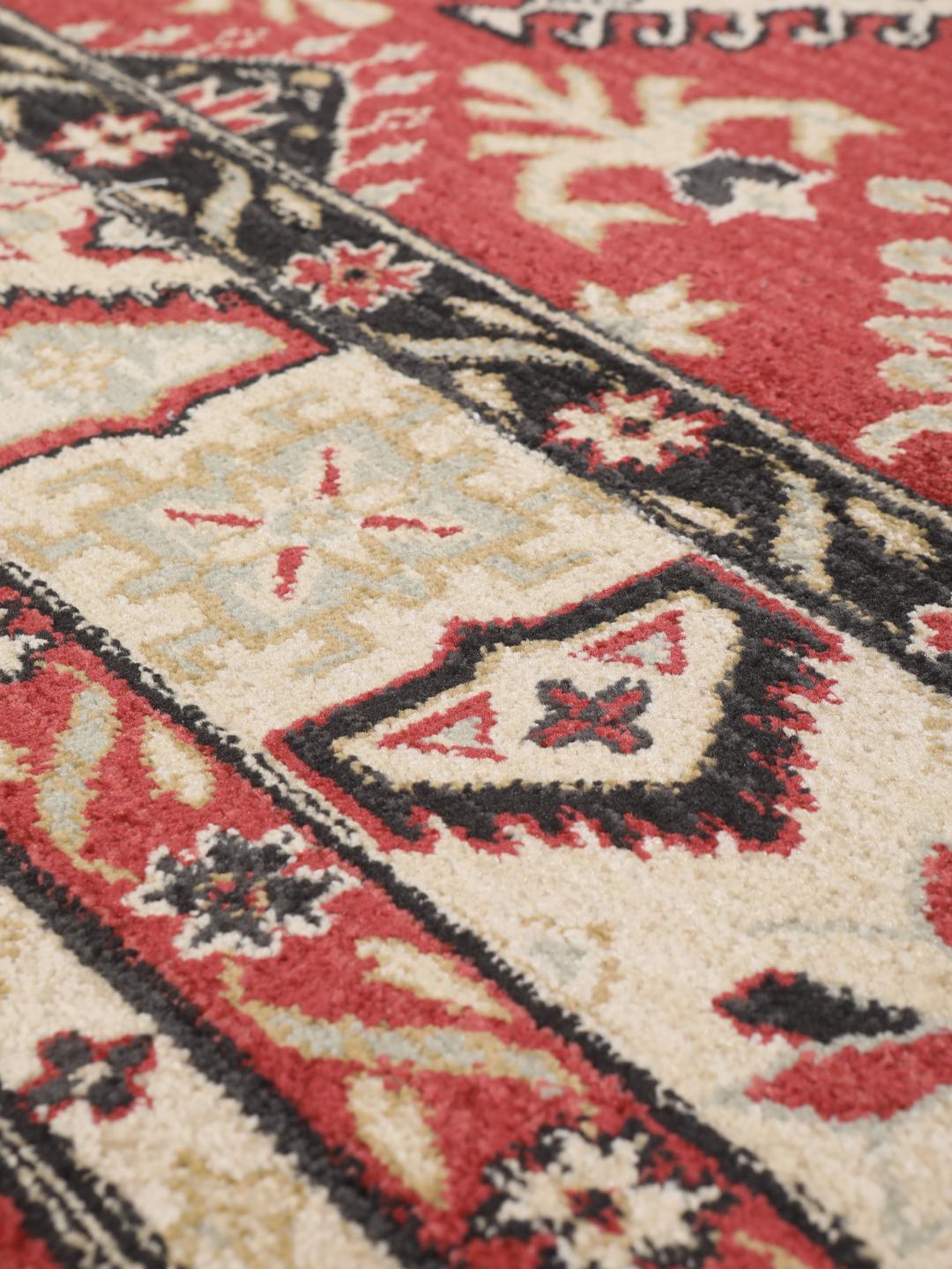 Et rødt og beige tæppe med et traditionelt mønstret design.