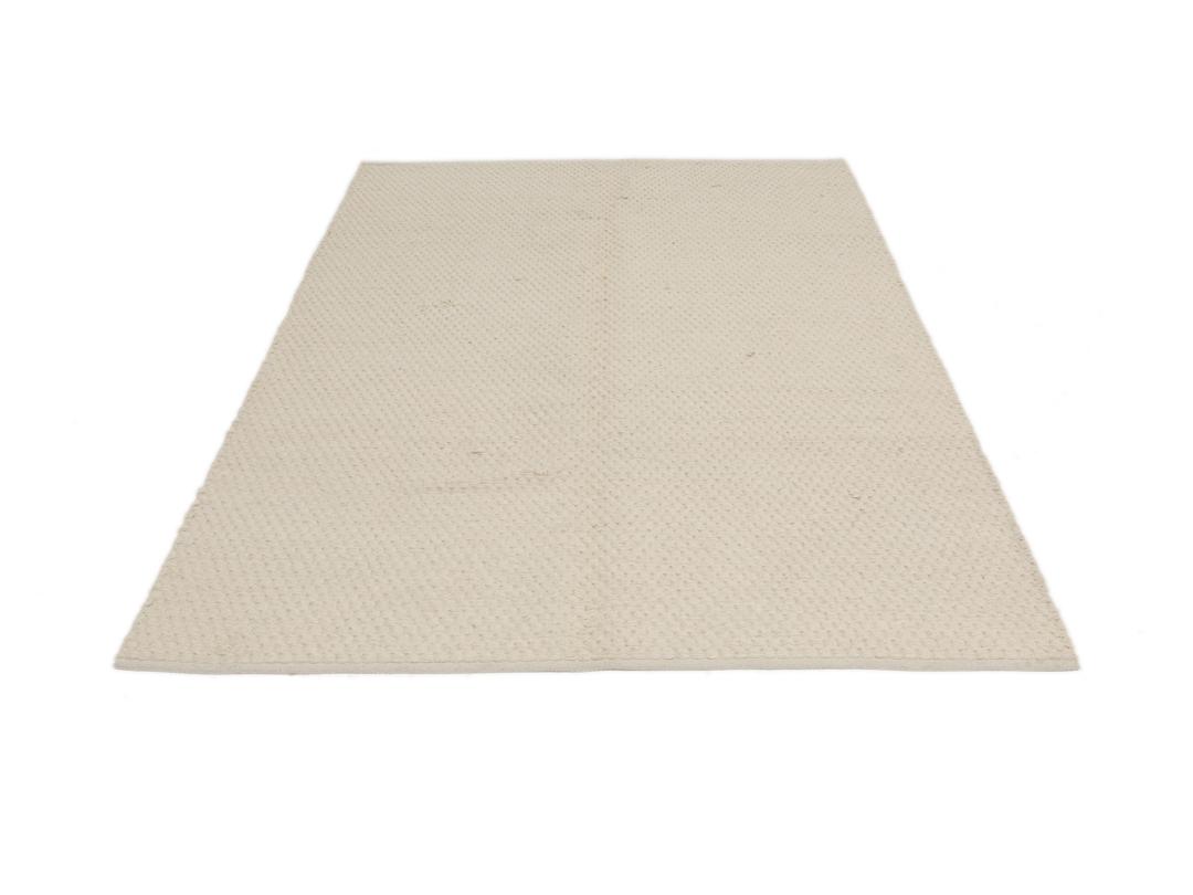 En minimalistisk, beige handvävd matta från Indien med en ren, texturerad yta.