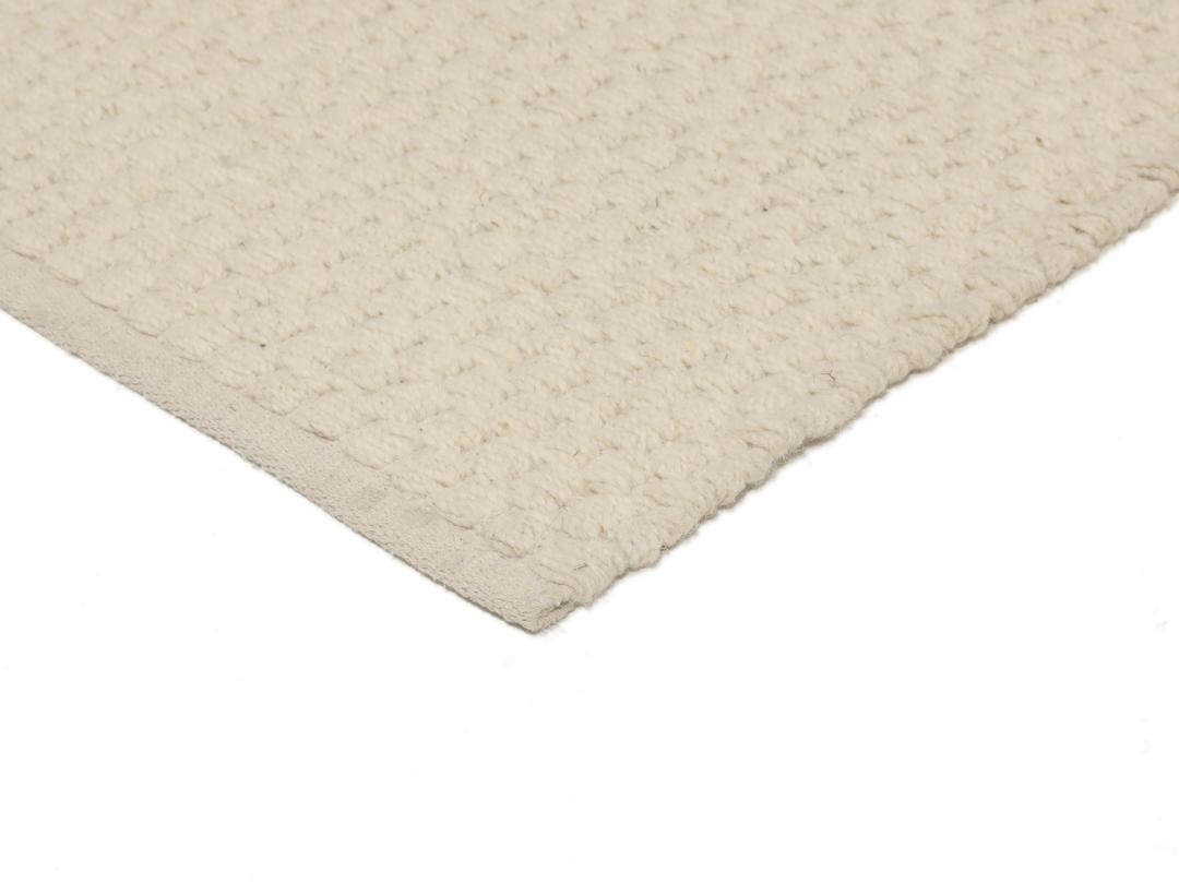 En minimalistisk, beige handvävd matta från Indien med en ren, texturerad yta.