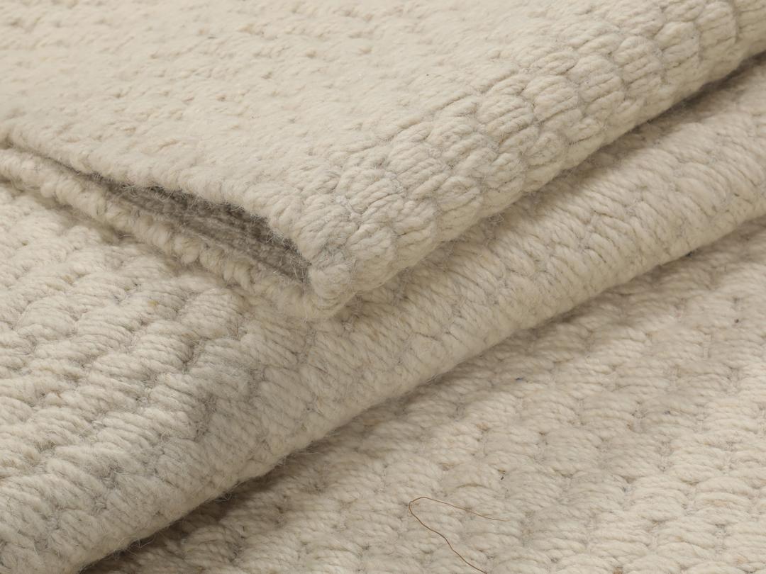 En minimalistisk, beige handvävd matta från Indien med en ren, texturerad yta.