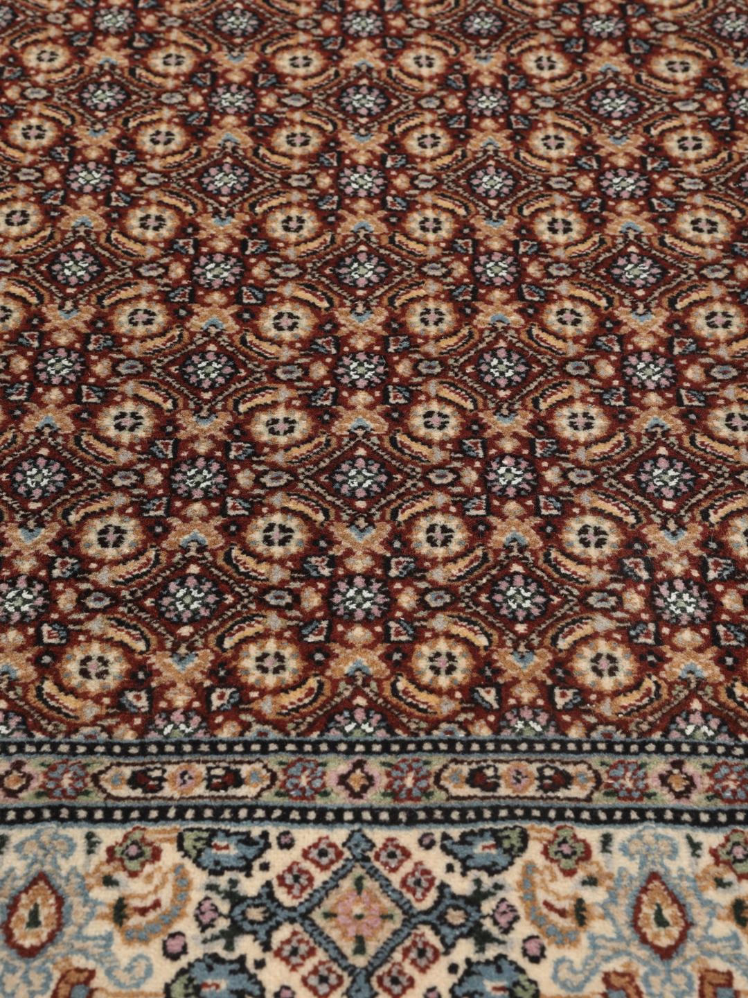 A hand-knotted Moud rug with traditional floral motifs in dark-red and blue tones.