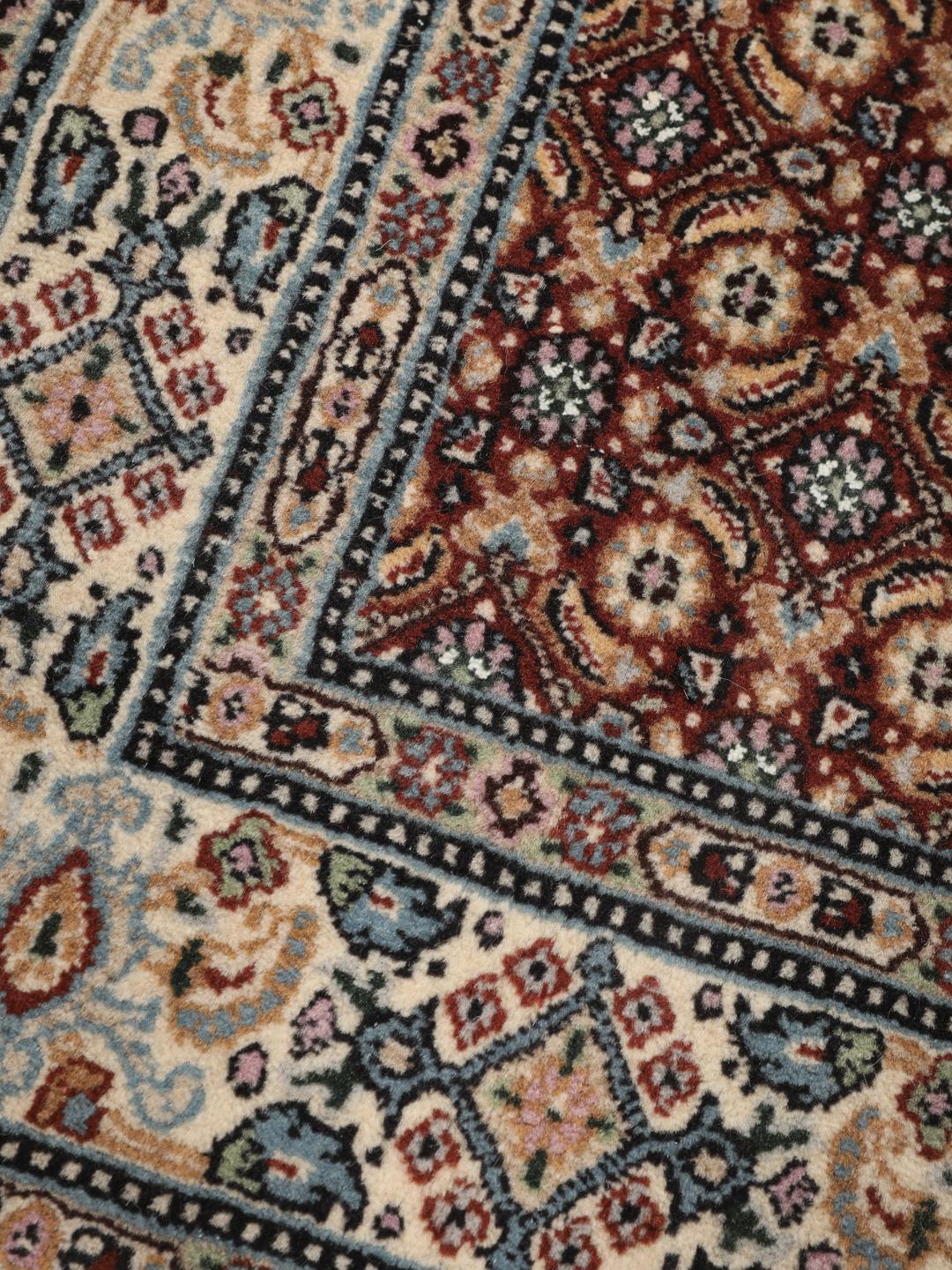 A hand-knotted Moud rug with traditional floral motifs in dark-red and blue tones.