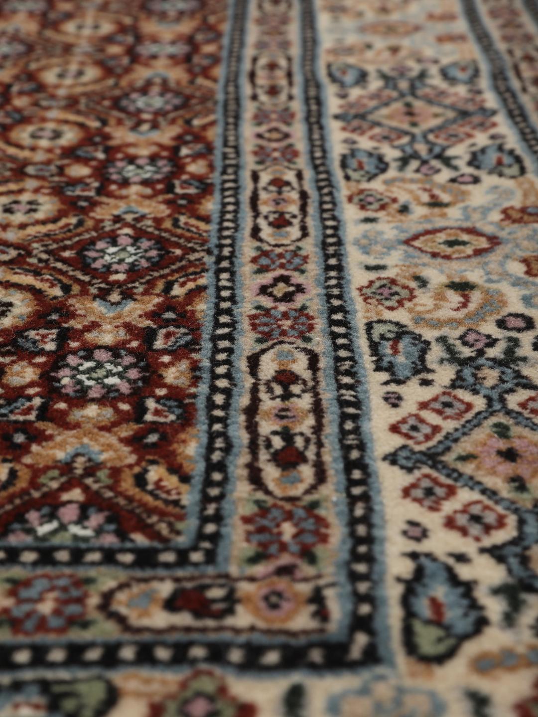 A hand-knotted Moud rug with traditional floral motifs in dark-red and blue tones.