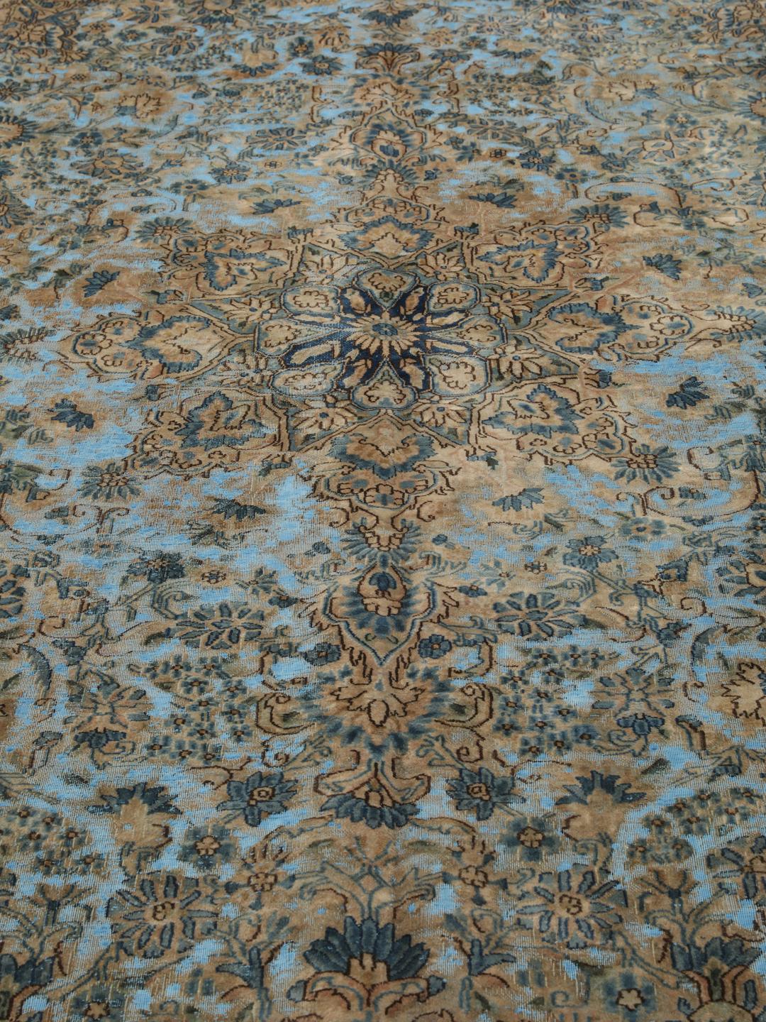 Een groot rechthoekig vintage kleed uit het Midden-Oosten met een bloemendesign in blauwe en bruine tinten.